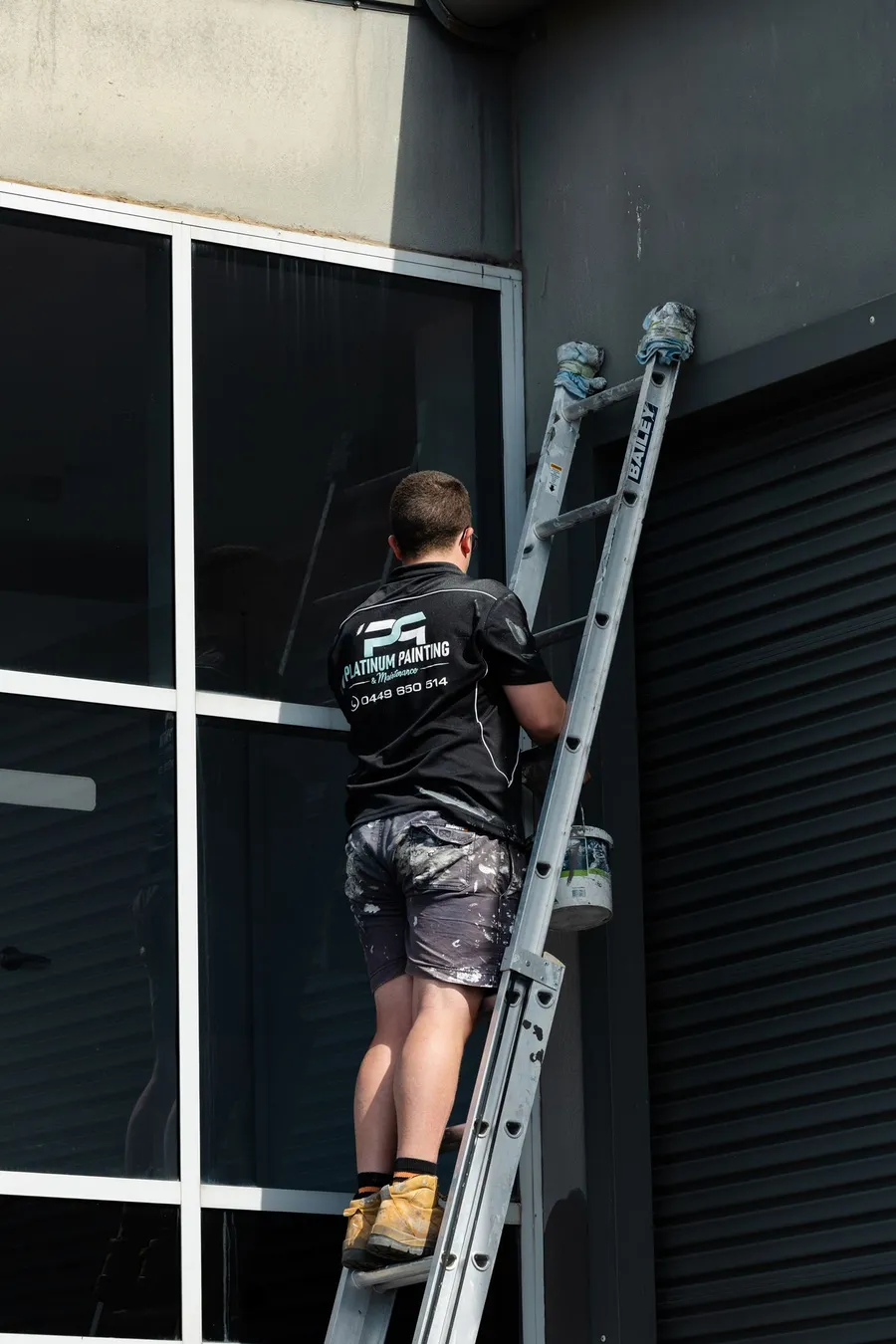 Platinum painter working from a ladder on a commercial exterior